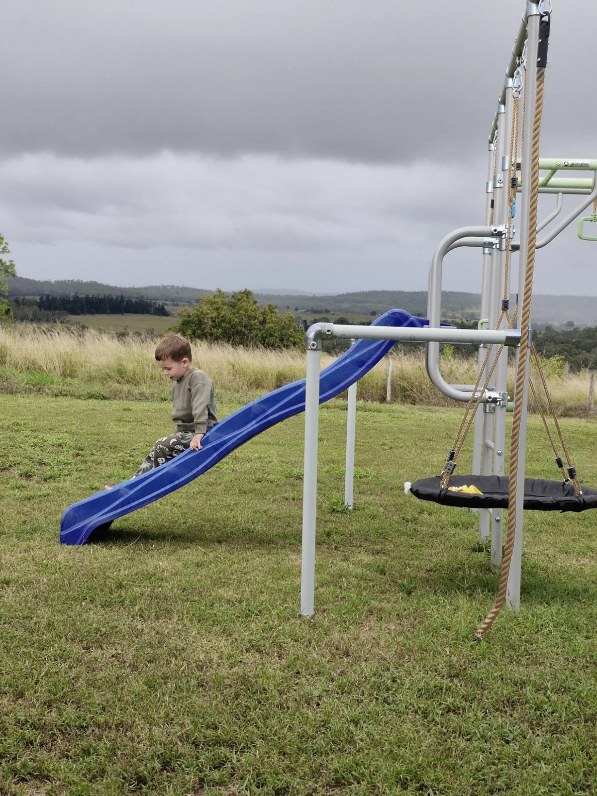 Growplay Slide Mount and slide beside a green monkey bar frame in a rural backyard — slide sold separately